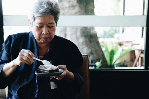 old asian elderly senior elder woman eating cheesecake at restaurant. mature retirement lifestyle
