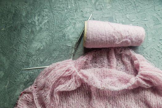 Knitting background flatlay. Bobbin of pink yarn, knitting needles, a knitted pullover on a concrete background, top view. Background about needlework and handicrafts, copy space