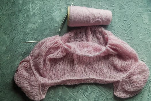 Knitting background flatlay. Bobbin of pink yarn, knitting needles, a knitted pullover on a concrete background, top view. Background about needlework and handicrafts, copy space