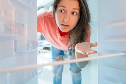 The girl is surprised at the empty refrigerator. Lack of food. Food delivery.