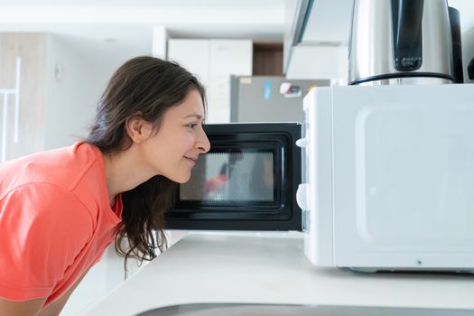 The girl warms food in the microwave. A quick snack.