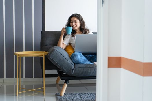 Beautiful girl sitting with a laptop on a sofa in a stylish room. Work from home. Work atmosphere in a good mood.