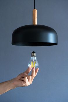 Close-up. A hand changes a light bulb in a stylish loft lamp. Spiral filament lamp. Modern interior decor