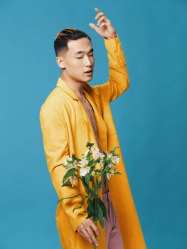 A young man of Asian appearance in a yellow coat with a bouquet of flowers gestures with his hands. High quality photo