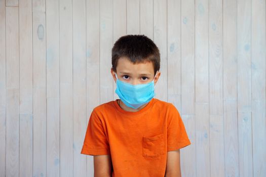 Portrait of a seven year old boy in a protective mask on a background of a wooden wall. Child in a medical mask looks directly into the camera. Childhood spoiled by Coronavirus Covid-19 pneumonia