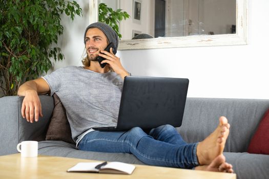 Handsome young business caucasian man working at home using laptop and talking with mobile phone