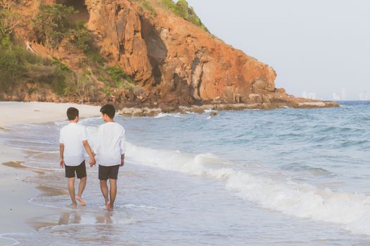 Back view homosexual portrait young asian couple walking with cheerful together on beach in summer, asia gay going tourism for leisure and relax with happiness in vacation at sea, LGBT legal concept.