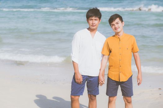 Homosexual portrait young asian couple standing together on beach in summer, asia gay holding hands going sea for leisure and relax with romantic and happy in vacation at sea, LGBT with legal concept.