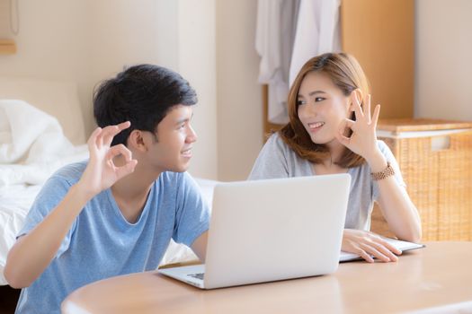 Beautiful portrait young asian couple working laptop with smile and happy sitting in bedroom, man and woman using notebook computer with excited and satisfied, business and success concept.