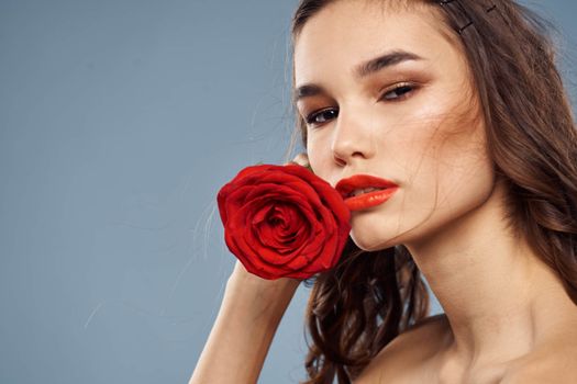 Portrait of a woman with a red rose in her hands on a gray background naked shoulders evening makeup. High quality photo