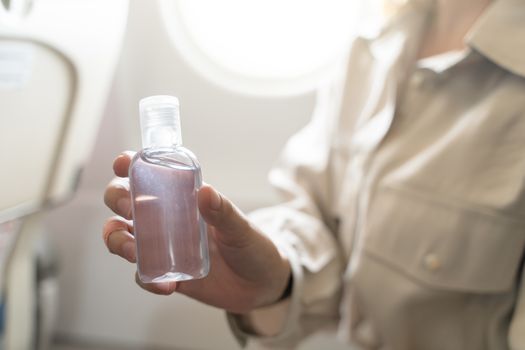 woman disinfects hands apply gel alcohol, on board of an airplane. New Normal, safety and travel transport during COVID-19 pandemic.