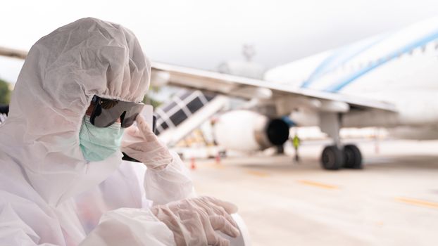 Person wearing protective suit , PPE with mask, sit on bus to entering airplane parking outside terminal in airport. during covid-19 virus pandemic , safety travel concept.