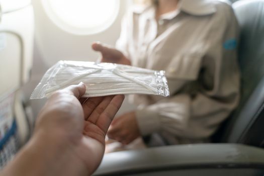 Hand sharing medical protective face mask on board of an airplane.