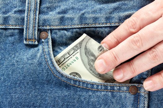 hand takes or putting in US dollar banknotes in the right front pocket of blue jeans. Concept of saving money or pocket expenses.