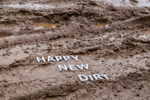 the words happy new dirt laid with silver metal letters on wet mud surface in diagonal perspective under cloudy autumn day light