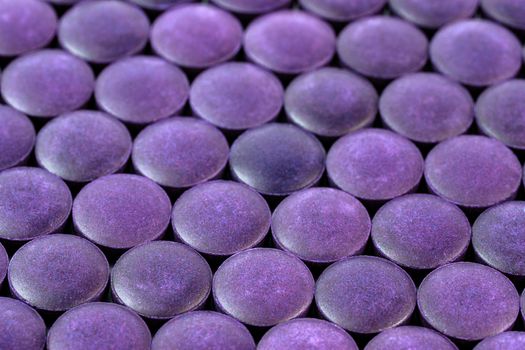 close-up background of many purple organic powder tablets laid tight in one layer on flat surface.