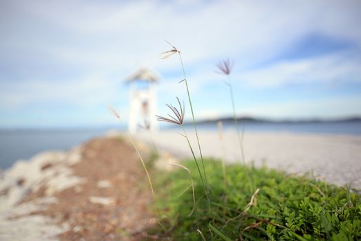 The grass that grows by the sea And there is a white lighthouse The sea and sky are a blurry background. In the eastern part of Thailand