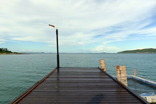 A dark brown wooden bridge extending into the sea, with a fish cage on its side.