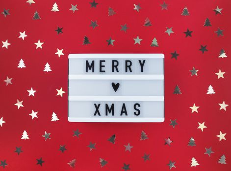 Merry Xmas greeting on light box and confetti on red background.