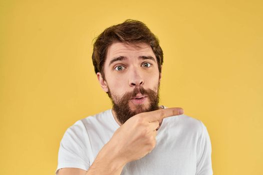 Bearded man emotions fun gesture with hands white t-shirt close-up yellow background. High quality photo