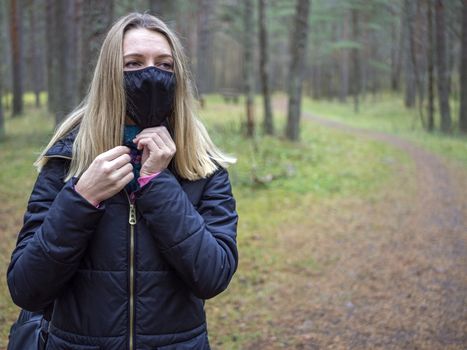 Beautiful european Women Wearing Protective Mask Outside Pretty young girl in medical black face mask in a forest. covid19 concept. modern reality. copy space. 2020, allergy. Autumn season. Copy space