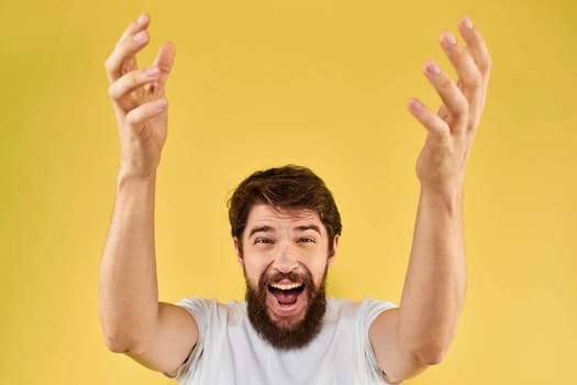 A man in a white t-shirt gestures with his hands lifestyle cropped view yellow background more fun. High quality photo