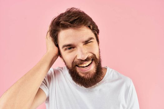 Bearded man in white t-shirt gesturing with hands facial expression close up pink background. High quality photo