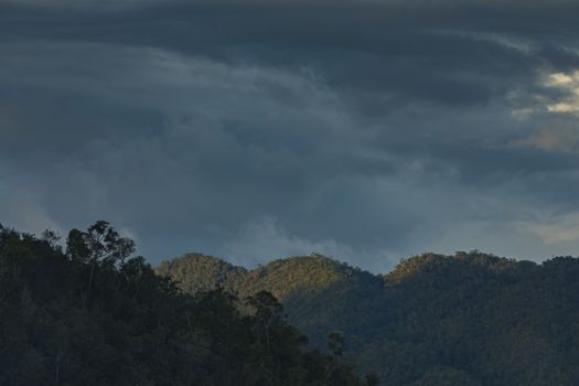 Beautiful clouds and sunset, over the mountains of Waiego Island, covered by thick tropical jungle, in the exotic Raja Ampat Islands, Indonesia, Southeast Asia.