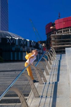 A little girl in yellow jeans stands against the background of the skyscrapers of the business center in Moscow city