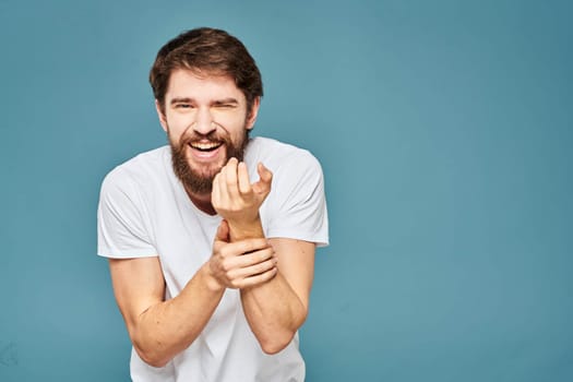 A bearded man in a white T-shirt gestures with his hands emotions blue background. High quality photo