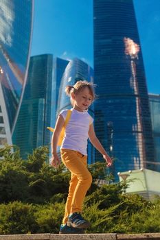 A little girl in yellow jeans stands against the background of the skyscrapers of the business center in Moscow city