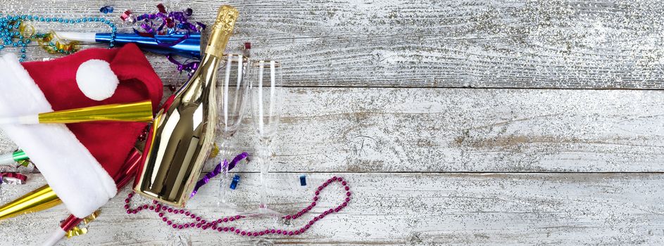 Happy New Year concept with a golden bottle of champagne, Santa hat, drinking glasses and party decorations 