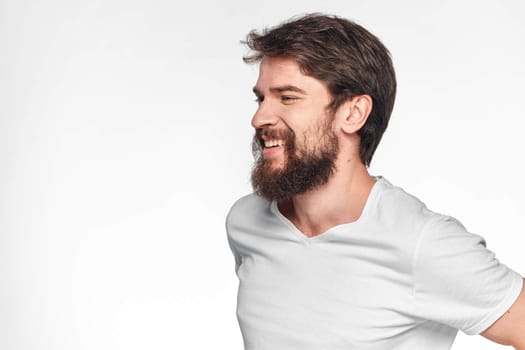 cheerful bearded man in a white t-shirt emotions gestures with his hands light background studio. High quality photo