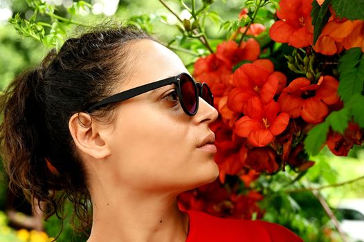 Beautiful young woman smelling red flowers in the park. Sarajevo, Bosnia and Herzegovina