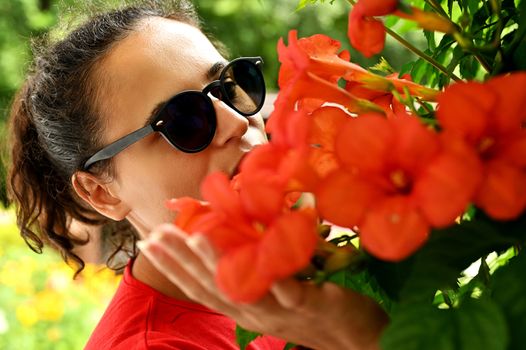 Beautiful young woman smelling red flowers in the park. Sarajevo, Bosnia and Herzegovina