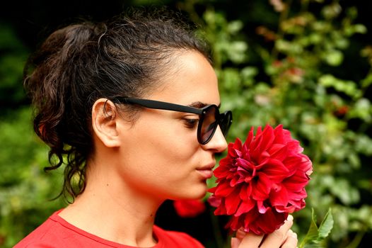 Beautiful young woman smelling red flower in the park. Sarajevo, Bosnia and Herzegovina