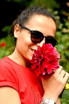 Beautiful young woman smelling red flower in the park. Sarajevo, Bosnia and Herzegovina