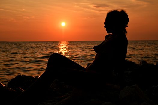 Romantic girl sitting on the pier near the water at sunset. Woman by the sea. Model on the beach on a background of sunlight.