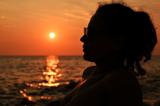 Romantic girl sitting on the pier near the water at sunset. Woman by the sea. Model on the beach on a background of sunlight.