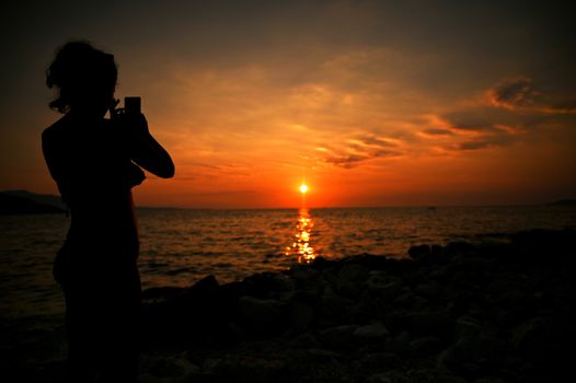 Romantic girl sitting on the pier near the water at sunset. Woman by the sea. Model on the beach on a background of sunlight.