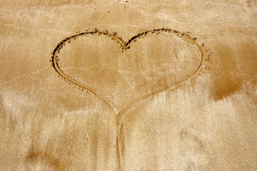 Hand drawn picture of the heart on wet beach sand.