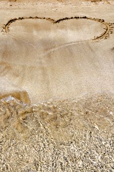 Hand drawn picture of the heart on wet beach sand.