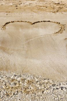 Hand drawn picture of the heart on wet beach sand.