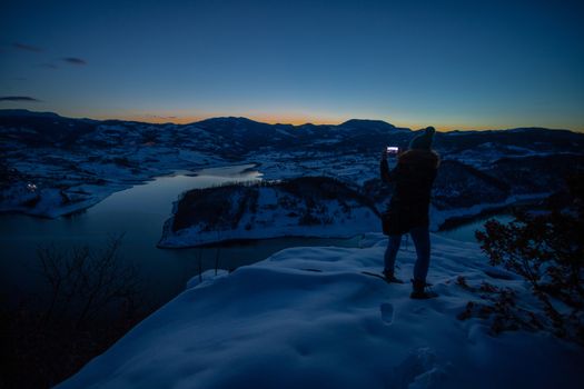 Photographers photographing winter lake mountain scene in sunset, alone in wilderness. Rovni, Valjevo, Serbia