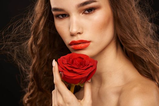 woman with a red rose on a dark background long hair makeup red lips. High quality photo