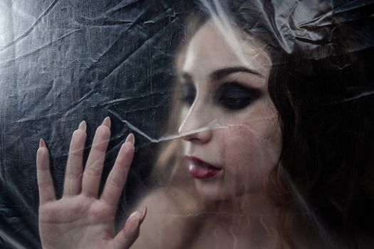 Young beauty sad woman trapped behind a plastic sheet as protection against COVID-19. Nicely fits for book cover