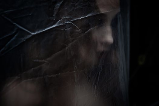 Young beauty sad woman trapped behind a plastic sheet as protection against COVID-19. Nicely fits for book cover