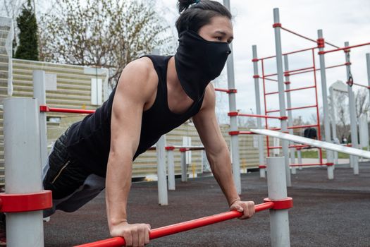 The guy is pushing up on the bars, in a black T-shirt and mask, in quarantine