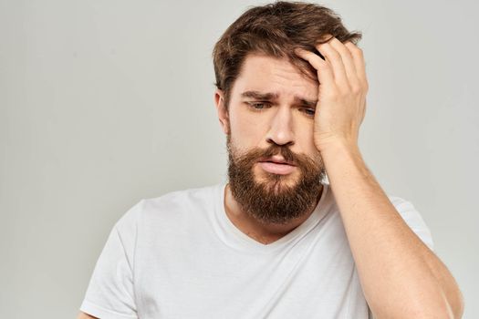 A man in a white t-shirt with a beard emotions displeased facial expression light background. High quality photo