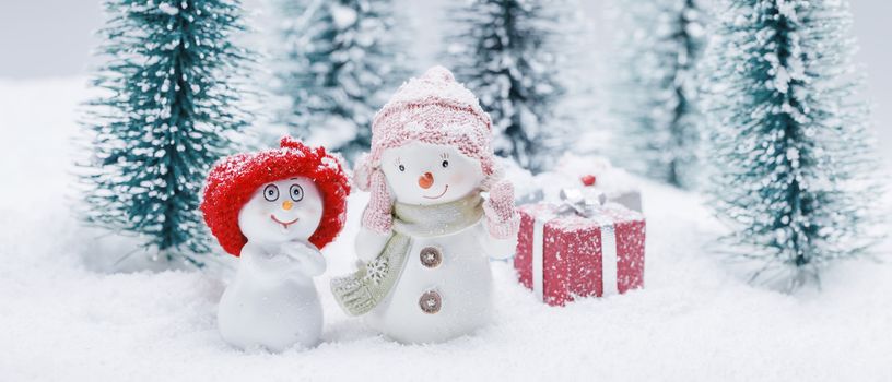 Two small cute snowmen friends with gift in forest under falling snow